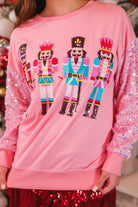 a lightweight pink long-sleeve top decorated with four vibrant nutcracker designs finished with dimensional beaded effect boots and accented by soft, shimmering velvet-sequin sleeves, a relaxed drop shoulder, and ribbed crew neckline, cuffs, and hem