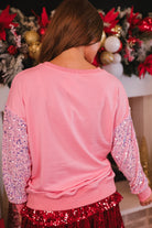 a lightweight pink long-sleeve top decorated with four vibrant nutcracker designs finished with dimensional beaded effect boots and accented by soft, shimmering velvet-sequin sleeves, a relaxed drop shoulder, and ribbed crew neckline, cuffs, and hem