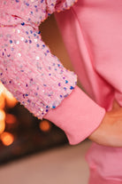 a lightweight pink long-sleeve top decorated with four vibrant nutcracker designs finished with dimensional beaded effect boots and accented by soft, shimmering velvet-sequin sleeves, a relaxed drop shoulder, and ribbed crew neckline, cuffs, and hem