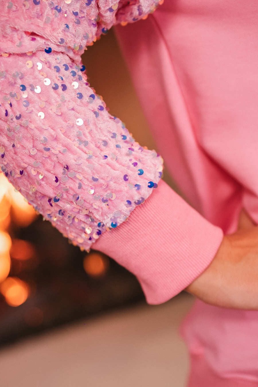 a lightweight pink long-sleeve top decorated with four vibrant nutcracker designs finished with dimensional beaded effect boots and accented by soft, shimmering velvet-sequin sleeves, a relaxed drop shoulder, and ribbed crew neckline, cuffs, and hem