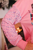 a lightweight pink long-sleeve top decorated with four vibrant nutcracker designs finished with dimensional beaded effect boots and accented by soft, shimmering velvet-sequin sleeves, a relaxed drop shoulder, and ribbed crew neckline, cuffs, and hem