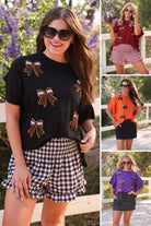 fluttery ruffle short-sleeve top with a mom crop length, sewn-on chenille football bow patches outlined in sequins on a soft, stretch-knit fabric in black, maroon, orange, and purple