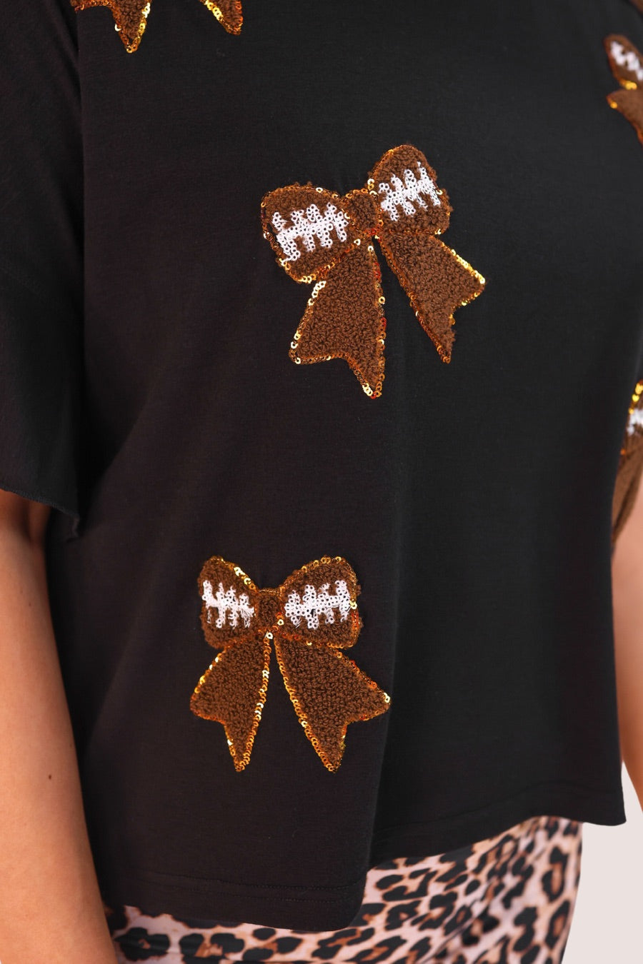 fluttery ruffle short-sleeve top with a mom crop length, sewn-on chenille football bow patches outlined in sequins on a soft, stretch-knit fabric in black