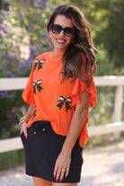 fluttery ruffle short-sleeve top with a mom crop length, sewn-on chenille football bow patches outlined in sequins on a soft, stretch-knit fabric in orange