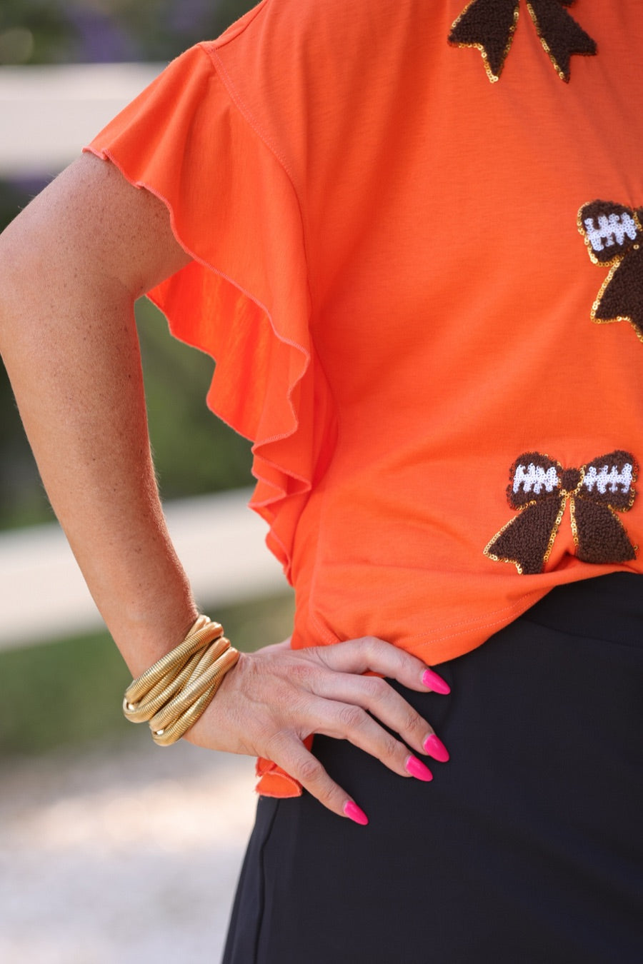fluttery ruffle short-sleeve top with a mom crop length, sewn-on chenille football bow patches outlined in sequins on a soft, stretch-knit fabric in orange