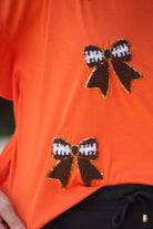 fluttery ruffle short-sleeve top with a mom crop length, sewn-on chenille football bow patches outlined in sequins on a soft, stretch-knit fabric in orange