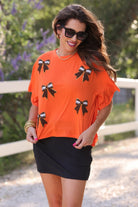 fluttery ruffle short-sleeve top with a mom crop length, sewn-on chenille football bow patches outlined in sequins on a soft, stretch-knit fabric in orange