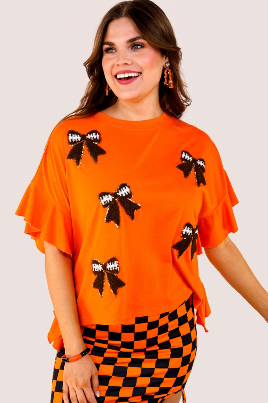fluttery ruffle short-sleeve top with a mom crop length, sewn-on chenille football bow patches outlined in sequins on a soft, stretch-knit fabric in orange