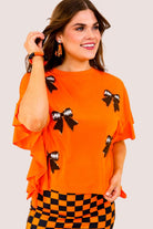 fluttery ruffle short-sleeve top with a mom crop length, sewn-on chenille football bow patches outlined in sequins on a soft, stretch-knit fabric in orange