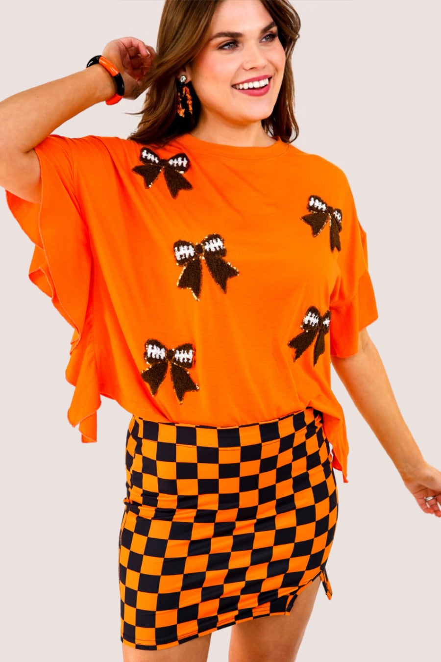 fluttery ruffle short-sleeve top with a mom crop length, sewn-on chenille football bow patches outlined in sequins on a soft, stretch-knit fabric in orange