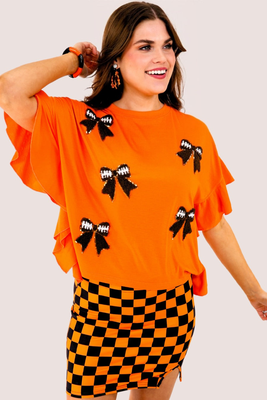 fluttery ruffle short-sleeve top with a mom crop length, sewn-on chenille football bow patches outlined in sequins on a soft, stretch-knit fabric in orange