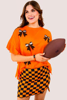 fluttery ruffle short-sleeve top with a mom crop length, sewn-on chenille football bow patches outlined in sequins on a soft, stretch-knit fabric in orange