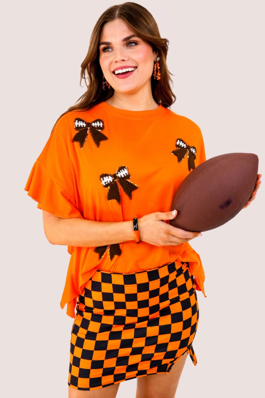 fluttery ruffle short-sleeve top with a mom crop length, sewn-on chenille football bow patches outlined in sequins on a soft, stretch-knit fabric in orange