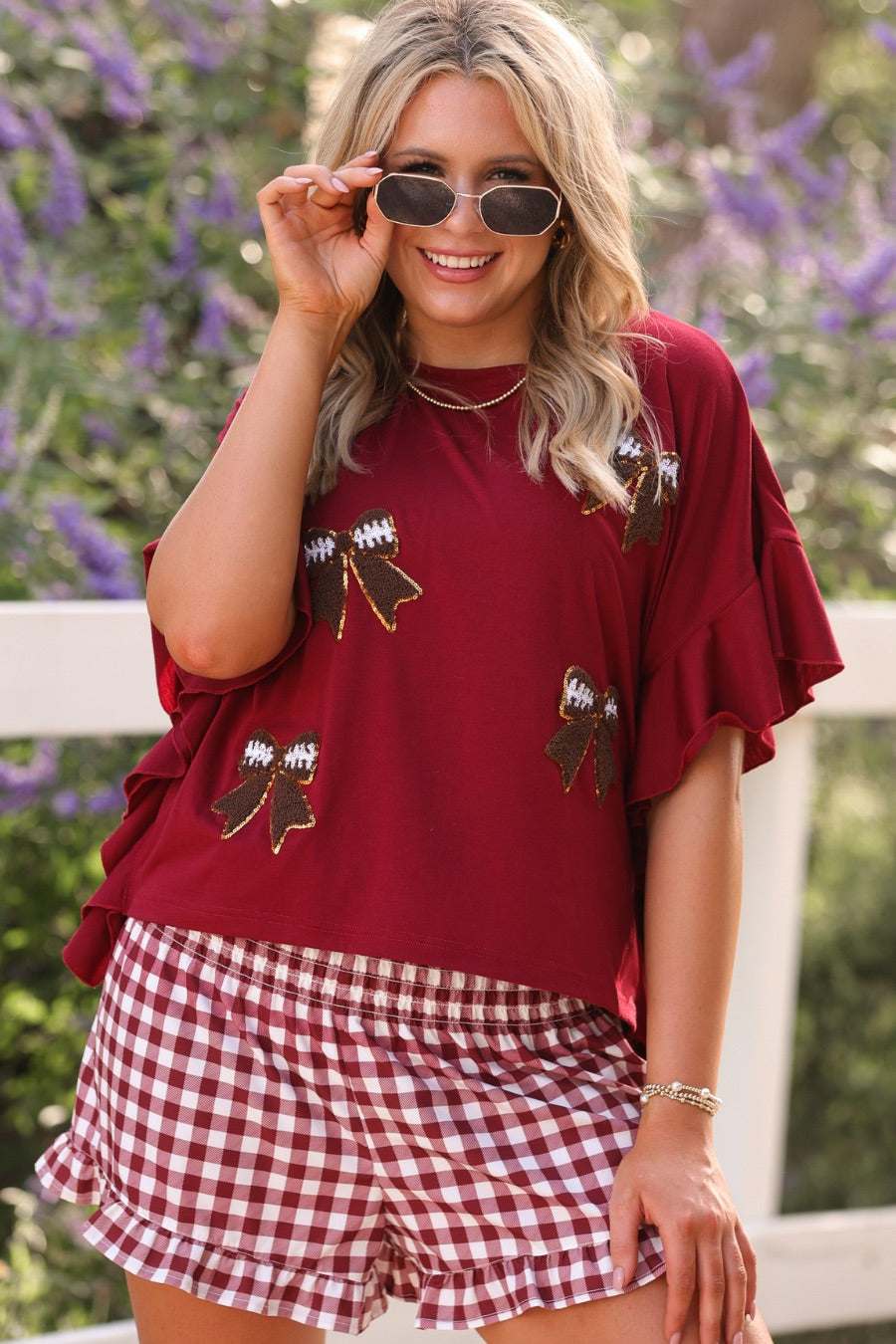 fluttery ruffle short-sleeve top with a mom crop length, sewn-on chenille football bow patches outlined in sequins on a soft, stretch-knit fabric in maroon