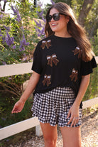 fluttery ruffle short-sleeve top with a mom crop length, sewn-on chenille football bow patches outlined in sequins on a soft, stretch-knit fabric in black