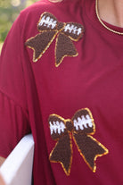 fluttery ruffle short-sleeve top with a mom crop length, sewn-on chenille football bow patches outlined in sequins on a soft, stretch-knit fabric in maroon