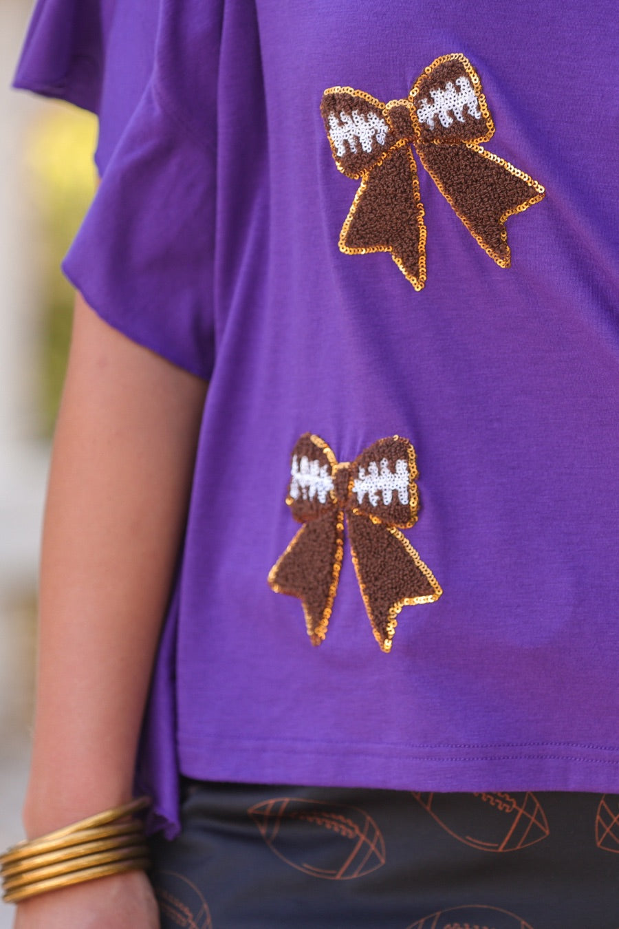 fluttery ruffle short-sleeve top with a mom crop length, sewn-on chenille football bow patches outlined in sequins on a soft, stretch-knit fabric in purple