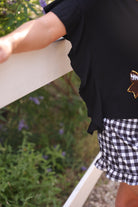 fluttery ruffle short-sleeve top with a mom crop length, sewn-on chenille football bow patches outlined in sequins on a soft, stretch-knit fabric in black