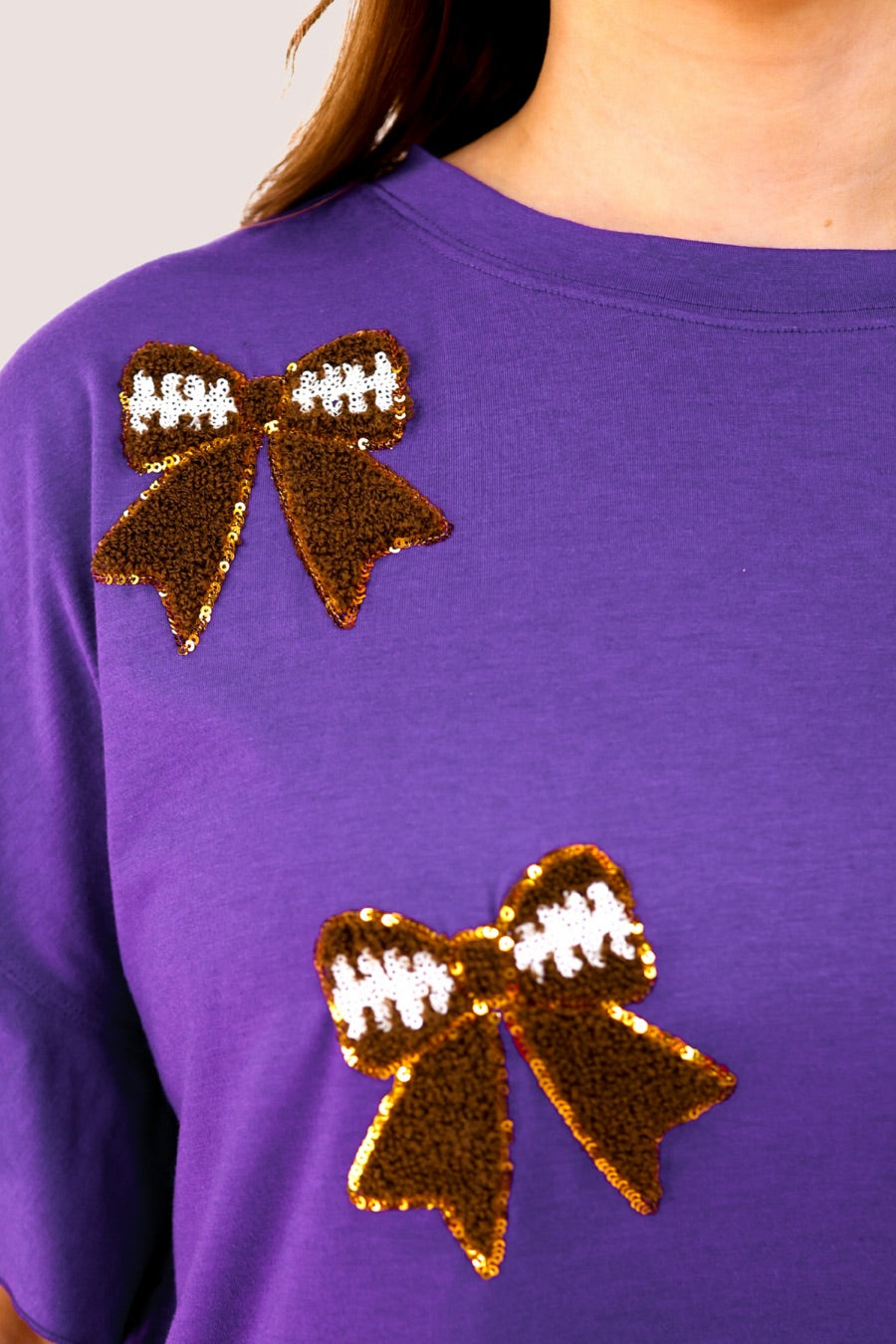 fluttery ruffle short-sleeve top with a mom crop length, sewn-on chenille football bow patches outlined in sequins on a soft, stretch-knit fabric in purple