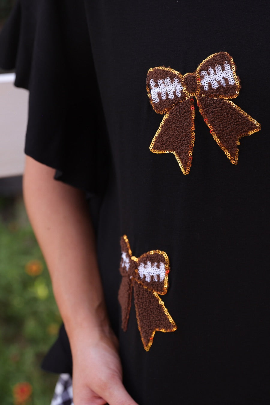 fluttery ruffle short-sleeve top with a mom crop length, sewn-on chenille football bow patches outlined in sequins on a soft, stretch-knit fabric in black