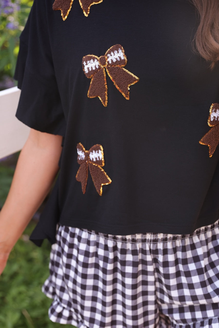 fluttery ruffle short-sleeve top with a mom crop length, sewn-on chenille football bow patches outlined in sequins on a soft, stretch-knit fabric in black