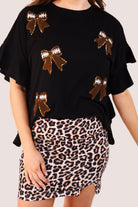 fluttery ruffle short-sleeve top with a mom crop length, sewn-on chenille football bow patches outlined in sequins on a soft, stretch-knit fabric in black