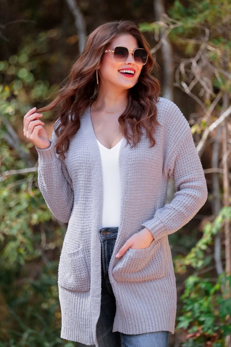  long sleeve cardigan made of a soft knit material with front pockets and a draped open front silhouette that ends in a straight hemline on a grey fabric