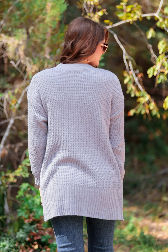 knit material, long sleeves, front pockets, & a draped open front silhouette that ends in a straight hemline