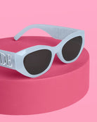 Sunglasses with a light blue frame and dark lenses on a pink platform