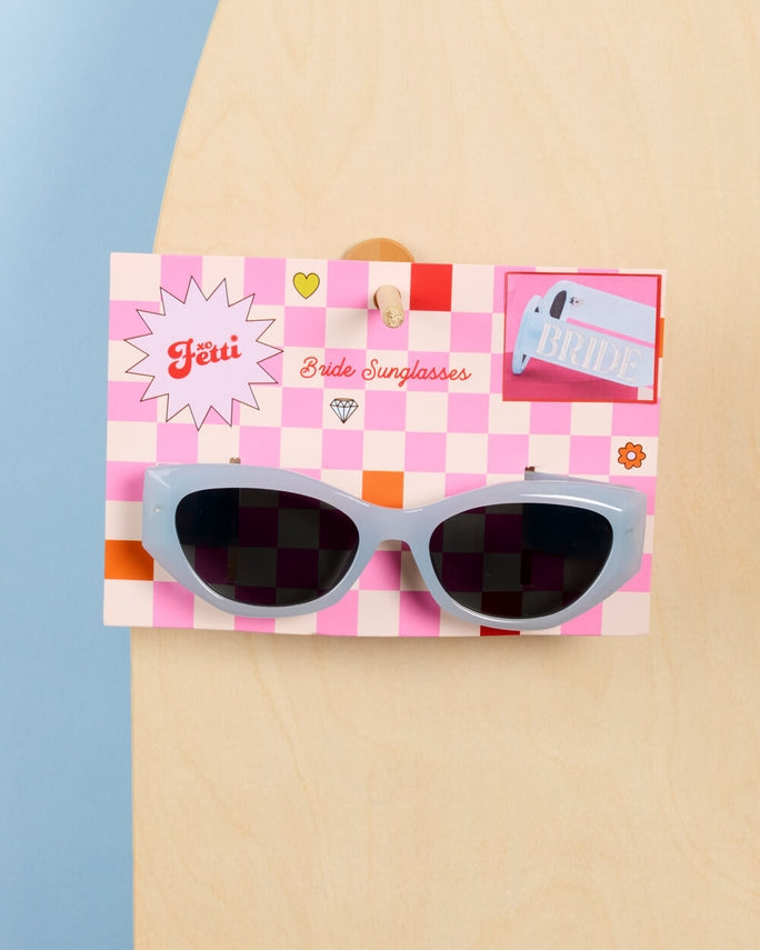 Checkered sunglasses with a pink packaging box on a beige and blue background