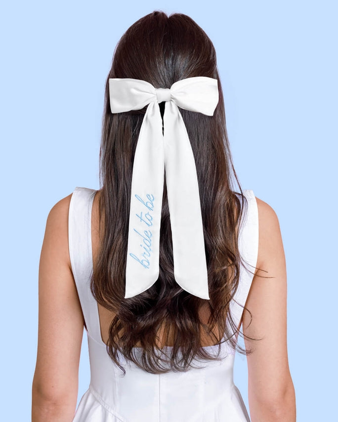 Woman with a white bow in her hair that says 'bride to be' on a light blue background