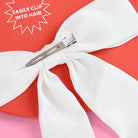 White hair bow with a clip on a red background