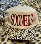a lightweight unisex two-tone hat with embroidered crimson 'SOONERS' lettering, cream structured front, curved contrasting black leopard bill, coordinating leopard top button, and adjustable snap-back closure