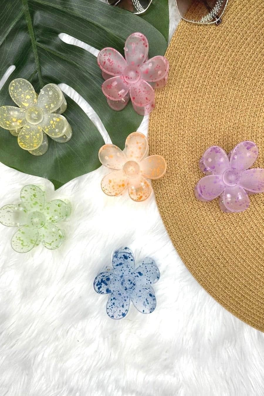 Colorful flower-shaped hair clips on a straw hat with green leaves and white fabric background