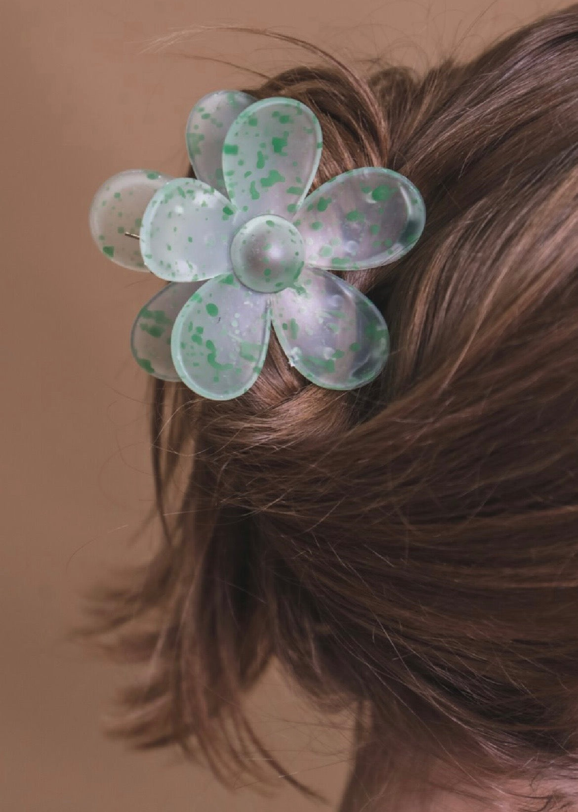 Green flower-shaped hair clip in a person's hair against a brown background