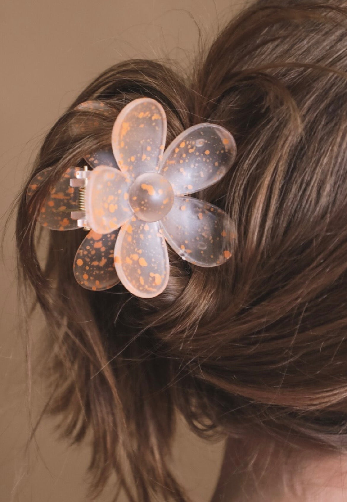 Orange flower-shaped hair clip in a person's hair against a brown background