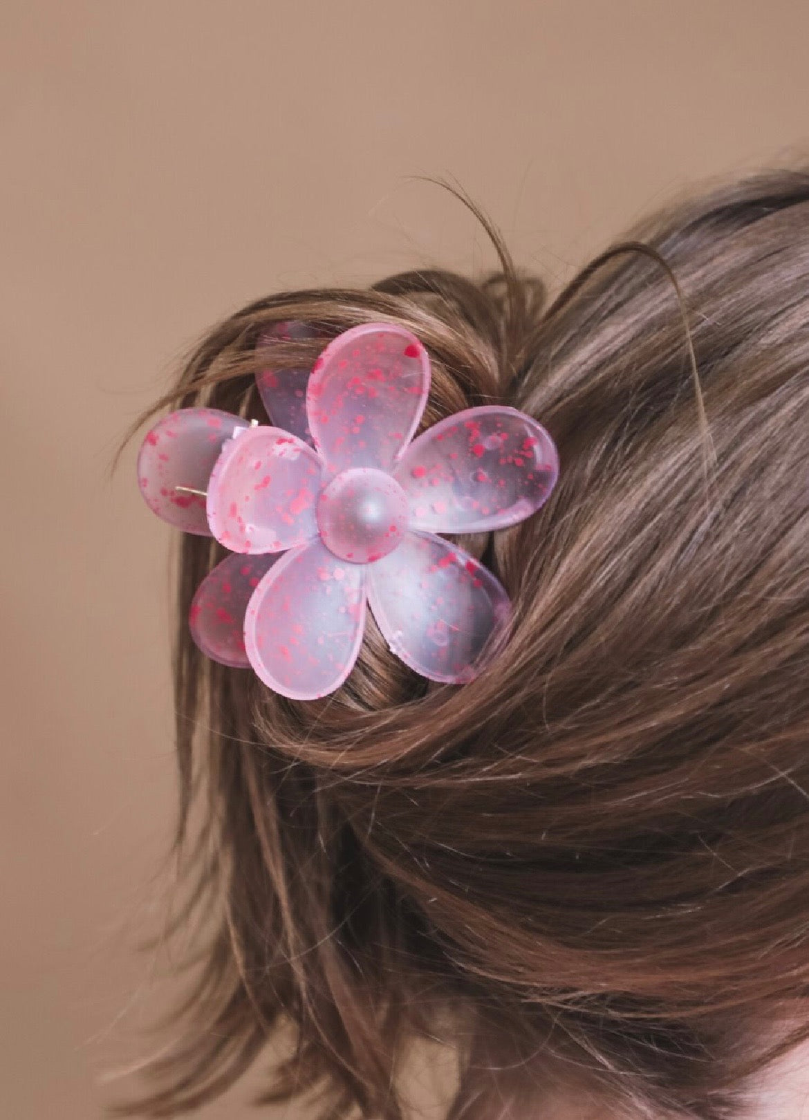 Pink flower-shaped hair clip in a person's hair against a brown background