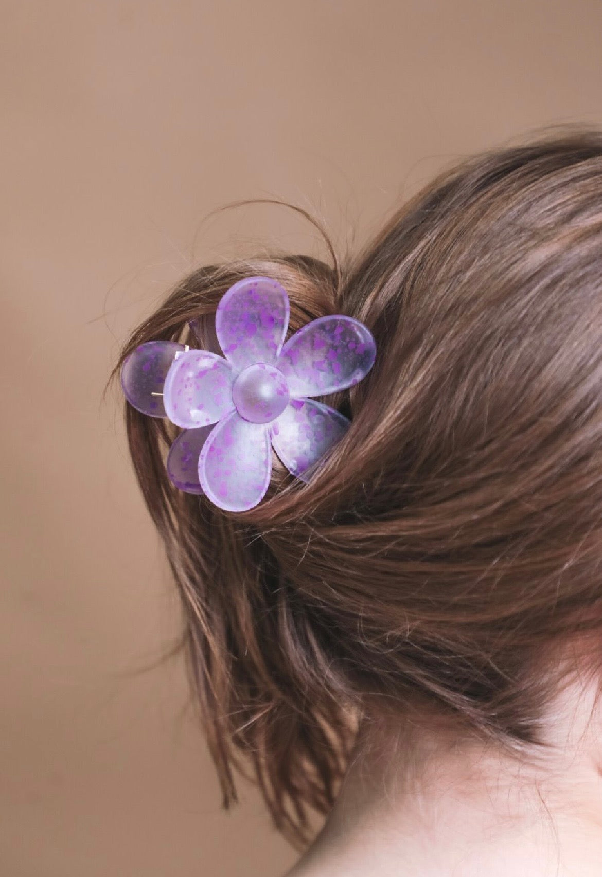 Purple flower-shaped hair clip in a person's hair against a brown background