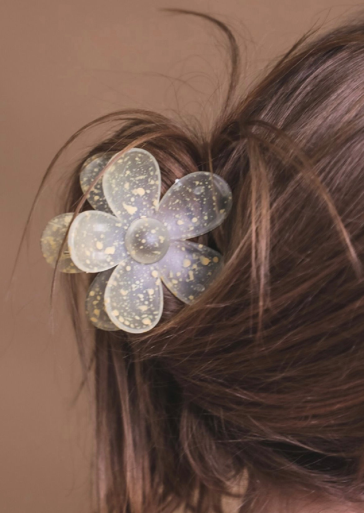 Yellow flower-shaped hair clip in a person's hair against a brown background