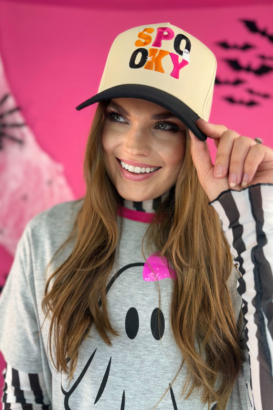 a classic black and cream adjustable canvas trucker hat with a cream structured front, a curved bill, and a snapback closure, finished with multicolor embroidered 'SPOOKY' lettering in black, orange, and pink, plus playful white embroidered mini bat, ghost, and spider accents