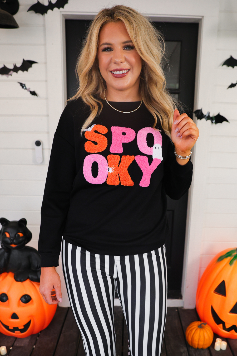 a black long-sleeve pullover made of ultra soft luxe material with bold plush chenille 'SPOOKY' patch lettering (orange and pink), white embroidered character accents (tiny bat, ghost and spider), ribbed cuffs, a banded hem, and a relaxed fit for a classic silhouette