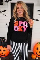 a black long-sleeve pullover made of ultra soft luxe material with bold plush chenille 'SPOOKY' patch lettering (orange and pink), white embroidered character accents (tiny bat, ghost and spider), ribbed cuffs, a banded hem, and a relaxed fit for a classic silhouette
