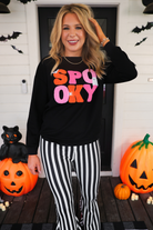 a black long-sleeve pullover made of ultra soft luxe material with bold plush chenille 'SPOOKY' patch lettering (orange and pink), white embroidered character accents (tiny bat, ghost and spider), ribbed cuffs, a banded hem, and a relaxed fit for a classic silhouette
