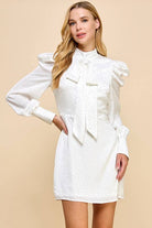 a white lined studded sheath dress with a high neckline accented with a decorative bow, puff shoulders, long cuffed sleeves, and a hidden rear zipper