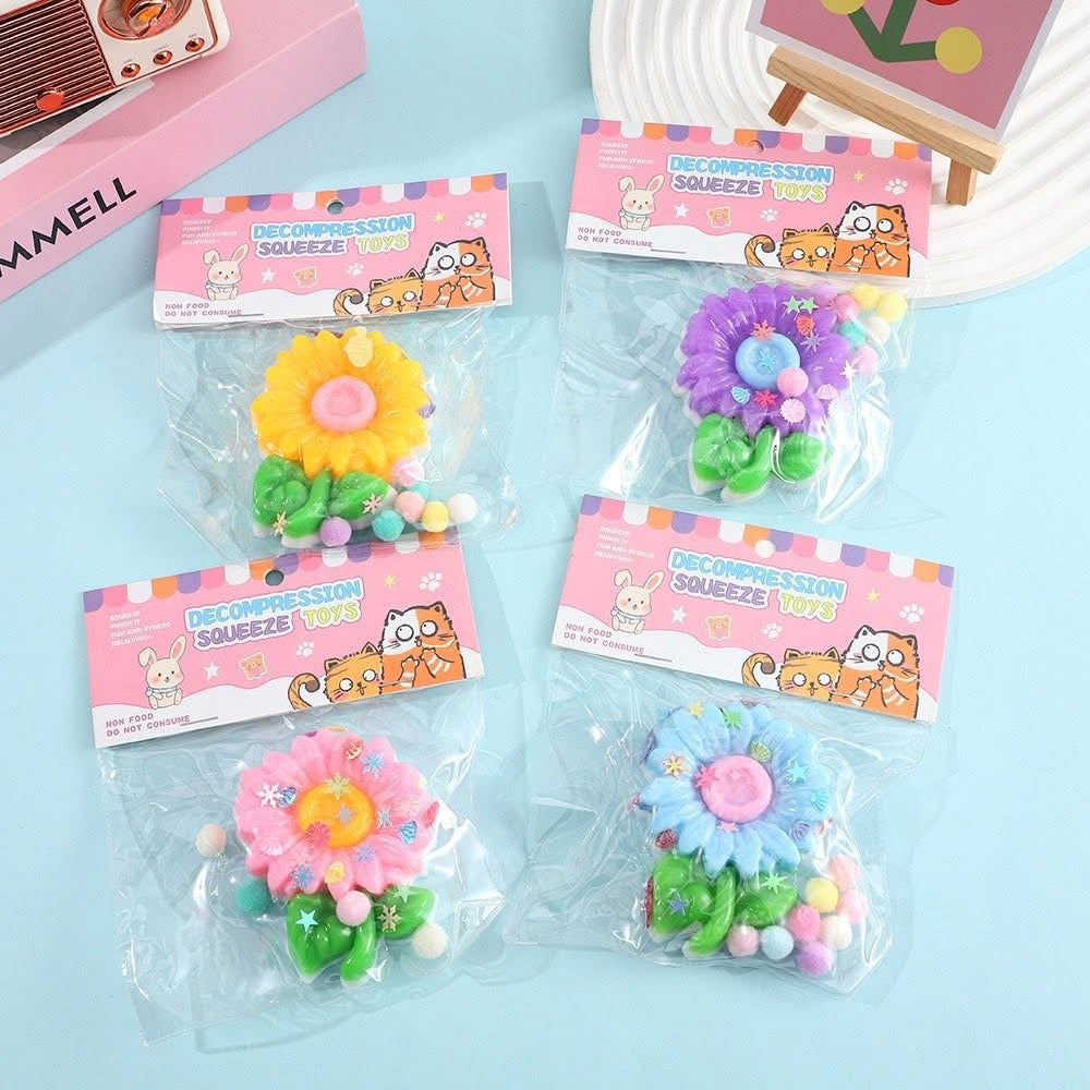 a flower-shaped decompression squishy toy with glossy petals, green leaves, mini decorative accents, and pastel pom poms in blue, pink, purple, and yellow