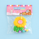 a yellow flower-shaped decompression squishy toy with glossy petals, green leaves, mini decorative accents, and pastel pom poms