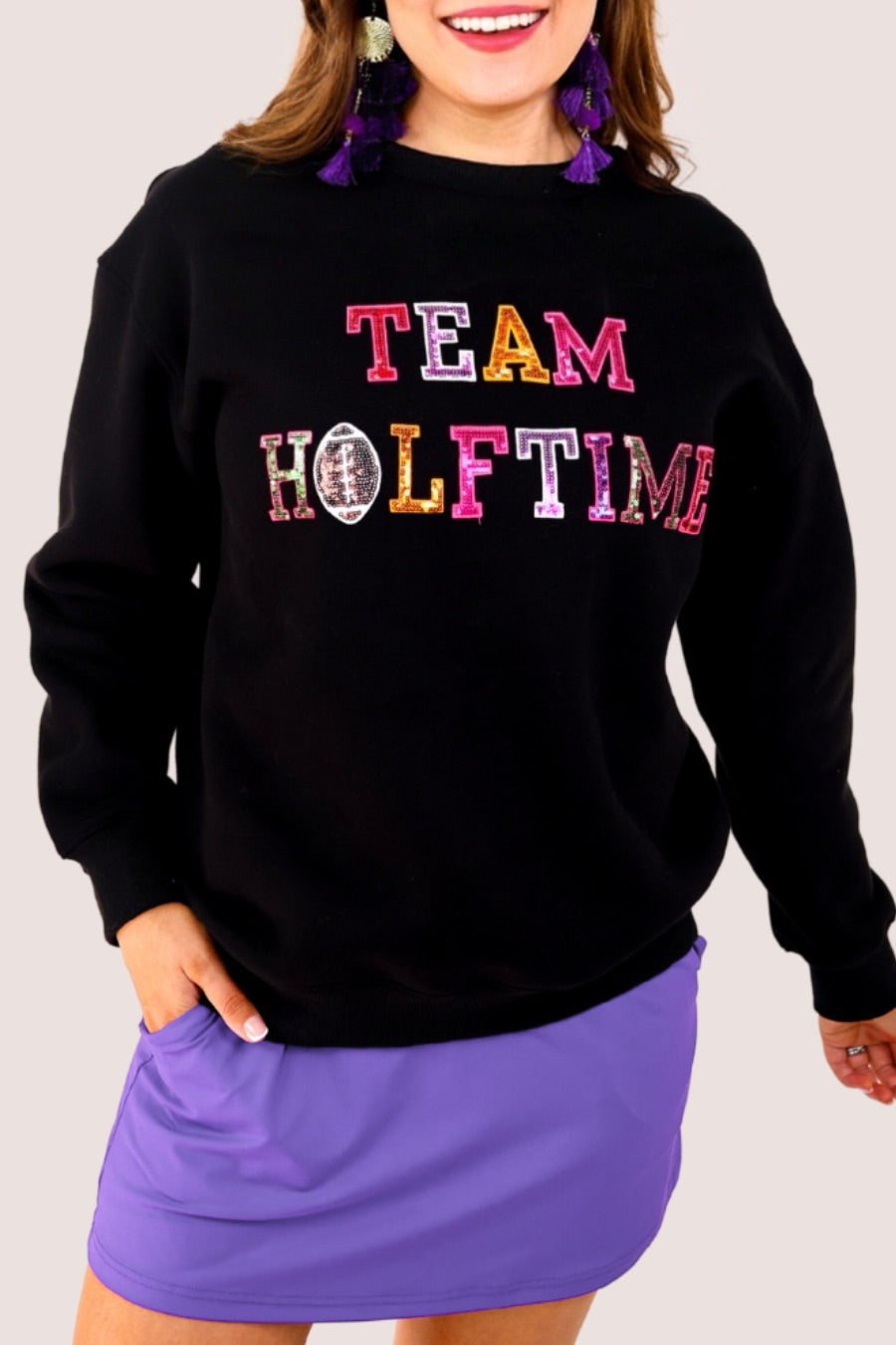 black long-sleeve sweatshirt made from soft mid-weight fabric with a crew neckline, straight hem, and bold multicolored varsity-style chenille patches that spell out 'TEAM HALFTIME' across the front chest