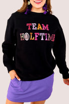 black long-sleeve sweatshirt made from soft mid-weight fabric with a crew neckline, straight hem, and bold multicolored varsity-style chenille patches that spell out 'TEAM HALFTIME' across the front chest