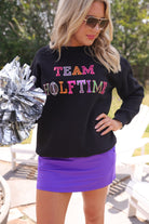 black long-sleeve sweatshirt made from soft mid-weight fabric with a crew neckline, straight hem, and bold multicolored varsity-style chenille patches that spell out 'TEAM HALFTIME' across the front chest