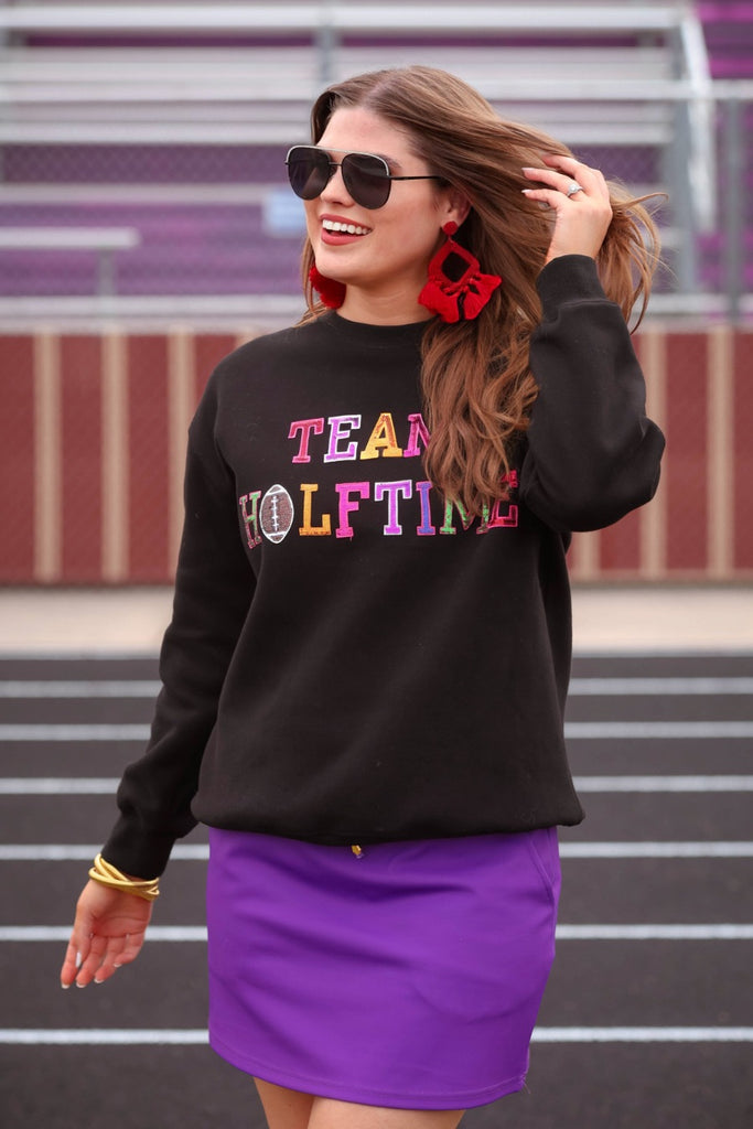 black long sleeve sweatshirt made from a midweight, soft material fabric with a crew neckline, straight hemline, and multicolored letter patches spelling out TEAM HALFTIME&nbsp;on the front